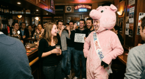 Futur marié déguisé en cochon rose assis au comptoir d'un bar bondé, portant une écharpe "FUTUR MARIÉ" et tentant de draguer en 2011 lors de son EVG.